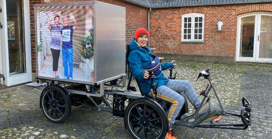 Kunstner vinker og cykler rundt om fjorden