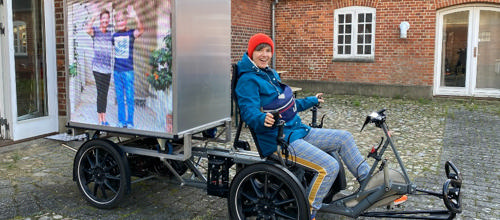 Kunstner vinker og cykler rundt om fjorden