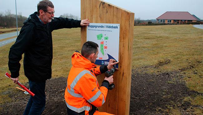 Formanden for Videbæk Borgerforening, Peter Vennevold, gav en hjælpende hånd, da Jacob Christensen fra Ringkøbing-Skjern Kommunes Vej- og Parkafdeling i går satte det første nye Til Salg-skilt op på ledige kommunale grunde i Videbæk