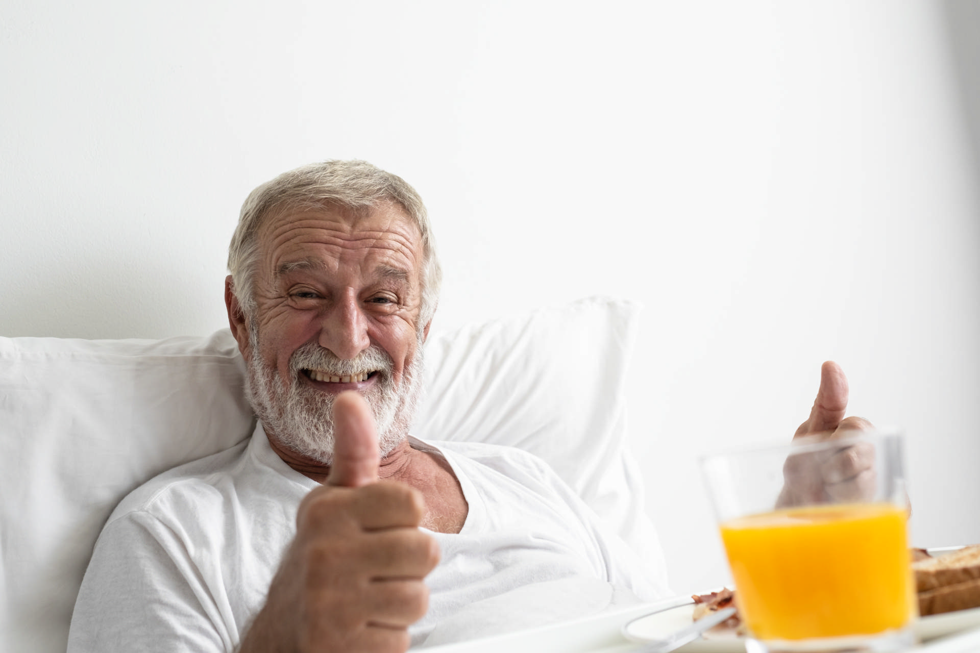 Dekorativt billede af en mand der ligger i en seng og giver en thumbs up til kameraet