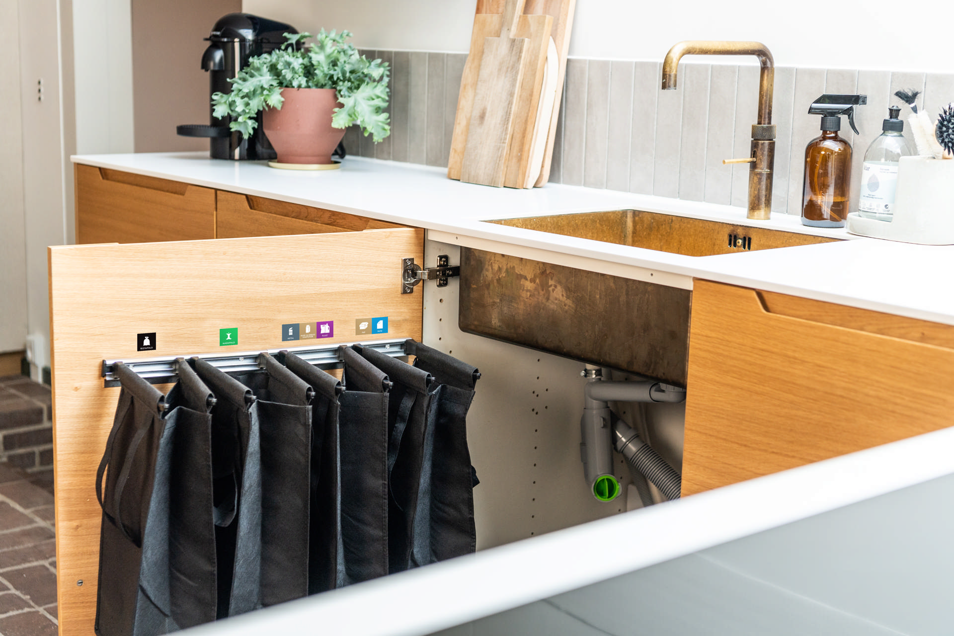 Køkkenvask med et åbent skab under. På skabslågen hænger der fire poser til sortering af affald. Klik for fuld størrelse.