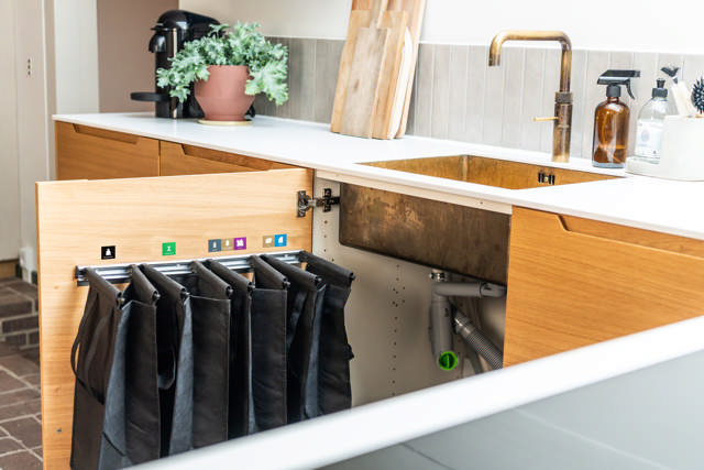 Køkkenvask med et åbent skab under. På skabslågen hænger der fire poser til sortering af affald. Klik for fuld størrelse.